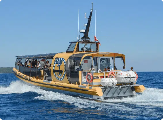 A yellow tour boat cruises on open water under a clear sky, carrying several people. The boat features large windows and safety equipment.