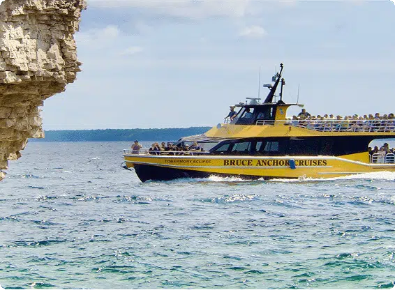 A boat labeled "Bruce Anchor Cruises" sails near a rocky shore, carrying several people under a cloudy sky.