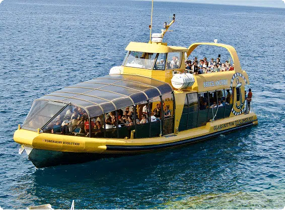 A yellow glass-bottom boat with people on board sails through blue water, likely for a tour or excursion, under clear skies.